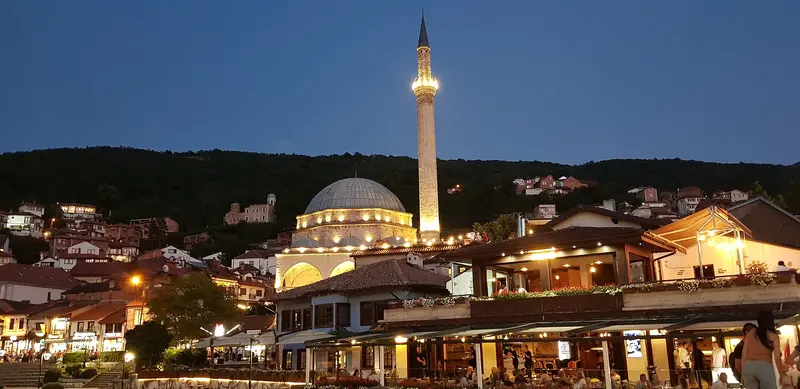 Sinan Pasha Mosque lit up at dusk above riverside cafes in Prizren